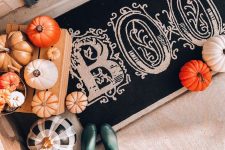 rustic front porch Halloween decor with natural pumpkins, a black and white rug and painted faux pumpkins