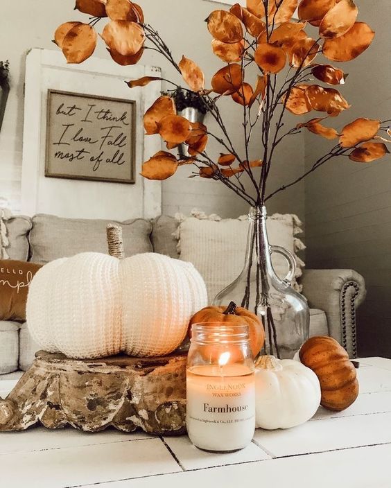 cozy rustic fall decor with faux pumpkins including a crochet one, a candle and dried leaves on branches