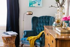 03 a colorful space with navy curtains, a bright rug, a blue velvet wingback chair, a wooden dresser