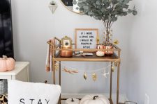 04 a modern fall bar cart with greenery in a vase, faux pumpkins, a fall leaf bunting and copper candleholders
