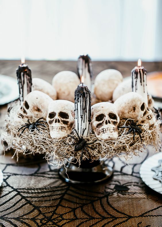 a Halloween centerpiece of a black stand, hay, skulls, spiders, candles with black drip is a stylish idea