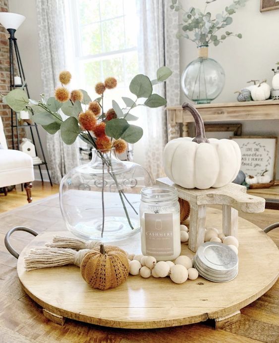 a simple and chic fall arrangement of a candle, wooden beads, faux pumpkins and a billy ball and greenery bouquet