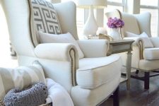 09 a neutral space done with elegant and cool white wingback chairs, pillows, a neutral side table and a lamp plus a basket with pillows
