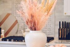 10 a stylish pastel fall arrangement of dried grasses and pink bunny tails, neutral and pink faux pumpkins and a candle in a glass