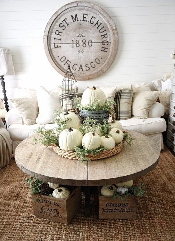 neutral fall decor of a basket tray with greenery, white pumpkins and some more pumpkins in crates under the table