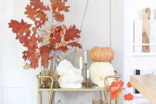 15 a modern elegant bar cart with stacked pumpkins, bright leaves in vases, candles and stained glasses is very chic