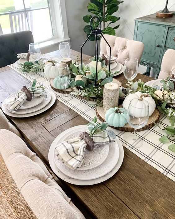 a neutral fall tablescape with a plaid runner and napkins, candles, white and green pumpkins and leaves