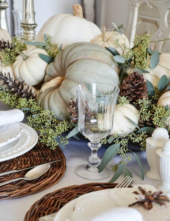 a neutral rustic table setting with woven placemats, white plates and napkins, all-natural pumpkins, greenery and pinecones