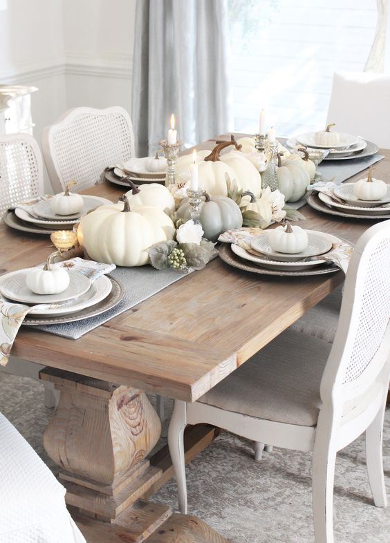a simple and elegant neutral tablescape with a grey runner and printed napkins, white and grey pumpkins, candles and faux blooms