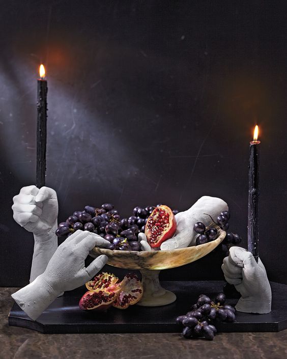 scary faux human hand candleholders with tall black candles and a bowl with fruits and matching hands