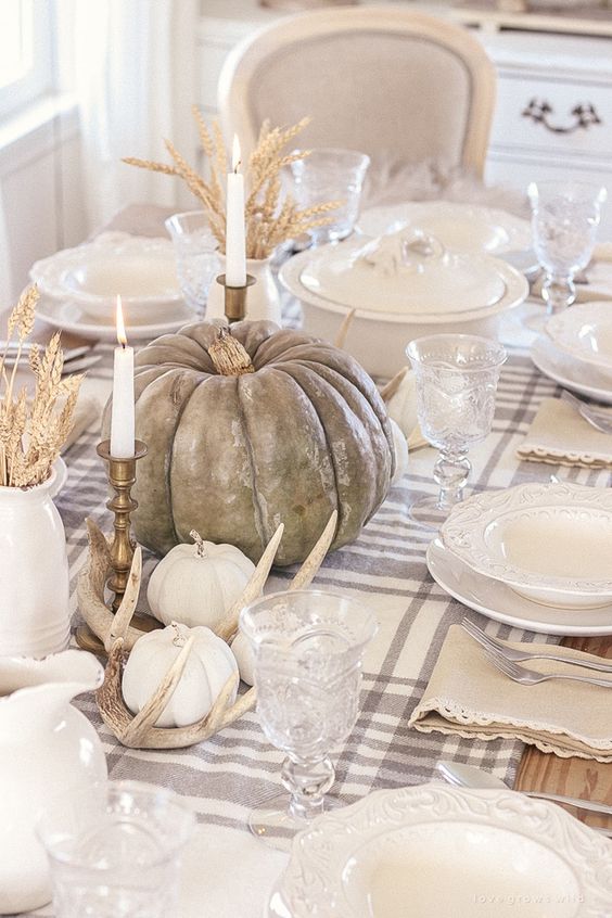 a very cozy fall tablescape with a plaid tablecloth, antlers, white pumpkins and candles and wheat in vases