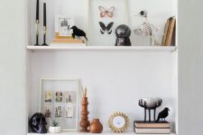 a Halloween bookshelf styled with black candles, skeletons, taxidermy, pumpkins and a skull in a cloche