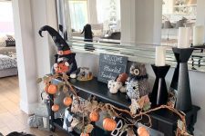 a black console with branches with pumpkins, leaves, white pumpkins, candles, witches’ hats is awesome for Halloween