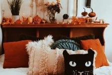 a boho Halloween bedroom with lights, fall leaves, macrame, boho Halloween pillows including a cat one and a sign