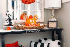 a bold Halloween console table with striped pillows, a basket tray with a jack-o-lantern, a pumpkin wreath and a pumpkin stack