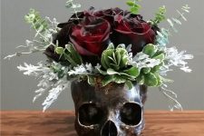 a bronze skull vase with eucalyptus, greenery and deep colored roses as a Halloween centerpiece