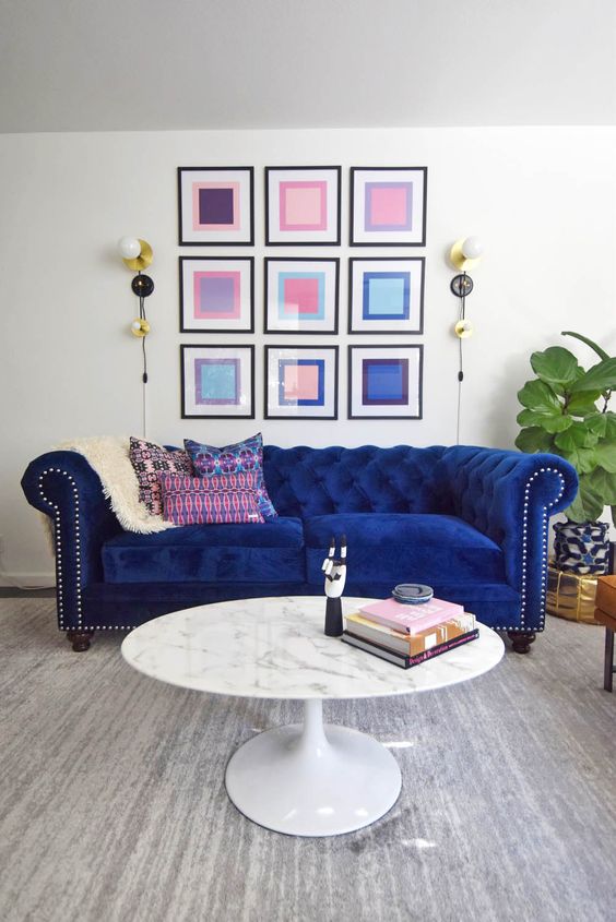 a colorful living room with a cobalt blue velvet Chesterfield sofa, a bold gallery wall, a marble table and a potted plant