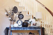 a console covered with a black spiderweb tablecloth, black and white pumpkins, ornaments and plates