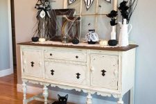 a creamy vintage console with a vintage window frame, a bunting, black faux blooms and lots of spiderweb
