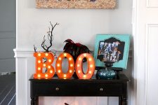 a dark stained console with faux pumpkins, a lit up pumpkin, marquee letters, branches and a photo