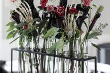 a gorgeous Halloween floral arrangement of red, pink and deep purple blooms, greenery, feathers and skeleton hands