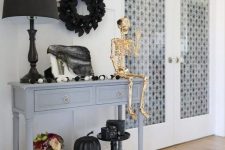 a grey console table with a black and white garland, a gold skeleton, a black flower wreath and pumpkins plus a giant skull