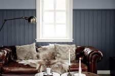 a grey living room with a brown leather Chesterfield sofa, wooden stools and a metal one, candles and a lamp