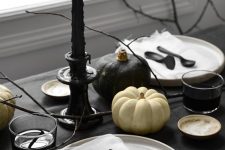 a minimalist Halloween table setting with black and white linens, black cutlery and candles, black and white pumpkins