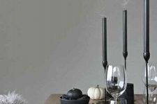 a minimalist Halloween tablescape with black candles in candleholders, black plates, cutlery, black and white pumpkins and acorns