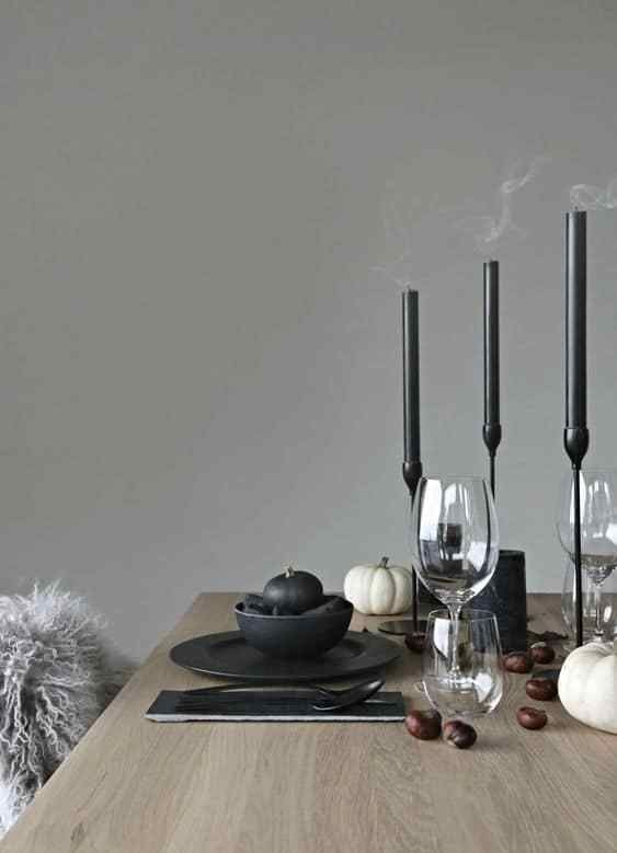 a minimalist Halloween tablescape with black candles in candleholders, black plates, cutlery, black and white pumpkins and acorns