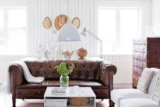a refined rustic living room with a brown leather Chesterfield sofa, a vintage apothecary cabinet and white chairs
