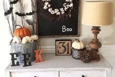 a simple rustic Halloween console with a cotton wreath, letters, pumpkins, bats on twigs, a vine ball and a vintage sign