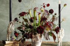 a skull vase with burgundy blooms, dark and usual leaves, greenery and black candles for Halloween