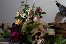 a skull with blush, burgundy, pink blooms, greenery, berries and moss for stylish Halloween decor