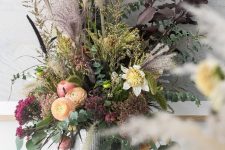 a stunning dark Halloween floral arrangement with eucalyptus, yellow and peachy blooms, dark leaves and purple grasses