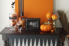 a stylish black and orange Halloween console with an artwork, faux pumpkins and glass jars with candies