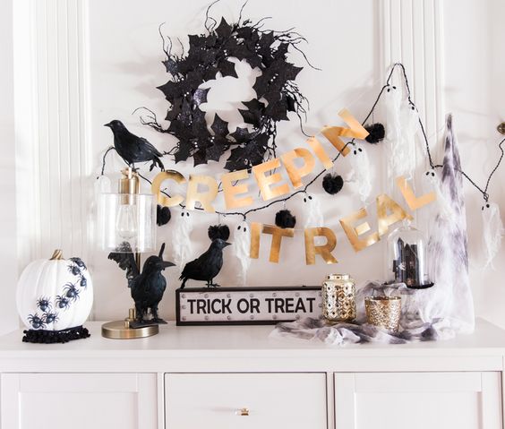 a stylish black, white and gold console with a bunting, a wreath, fake birds and a pumpkin with spiders