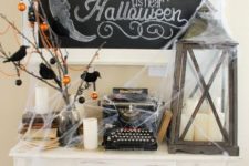 a vintage Halloween console with branches with blackbirds, ornaments, a candle lantern and lots of spiderweb
