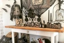 a vintage farmhouse console with lots of bats and birds, spiderweb, vintage artworks and signs and black candles