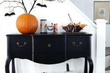 an elegant black console table with white pumpkins, an orange pumpkin as a vase, black branches with bats and bat candleholders