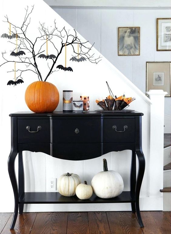 an elegant black console table with white pumpkins, an orange pumpkin as a vase, black branches with bats and bat candleholders