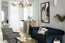 an exquisite living room in neutrals made bold with a navy velvet Chesterfield sofa, a gold table and printed chair and ottoman