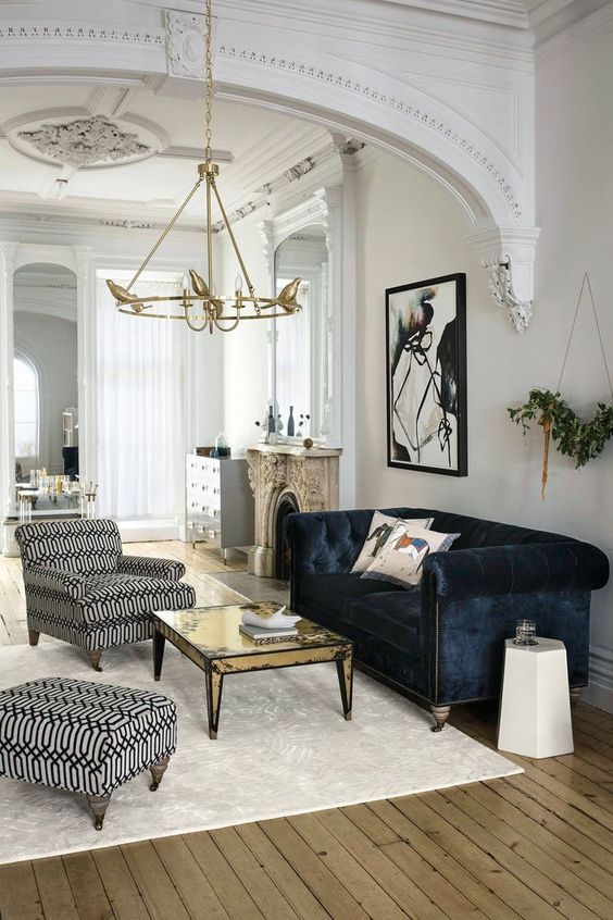 an exquisite living room in neutrals made bold with a navy velvet Chesterfield sofa, a gold table and printed chair and ottoman