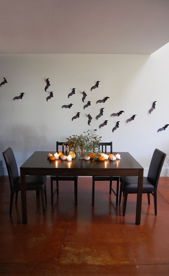 black paper bats on the wall, candles, mini pumpkins and a greenery arrangement for minimal Halloween styling