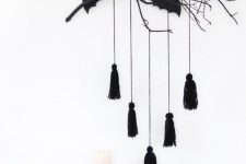 minimalist Halloween styling with a black branch with bats and tassels, mini pumpkins and a white candle in a candeholder
