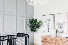 06 an airy and welcoming neutral nursery with a black crib, a grey paneled wall, a potted plant and a cool dresser