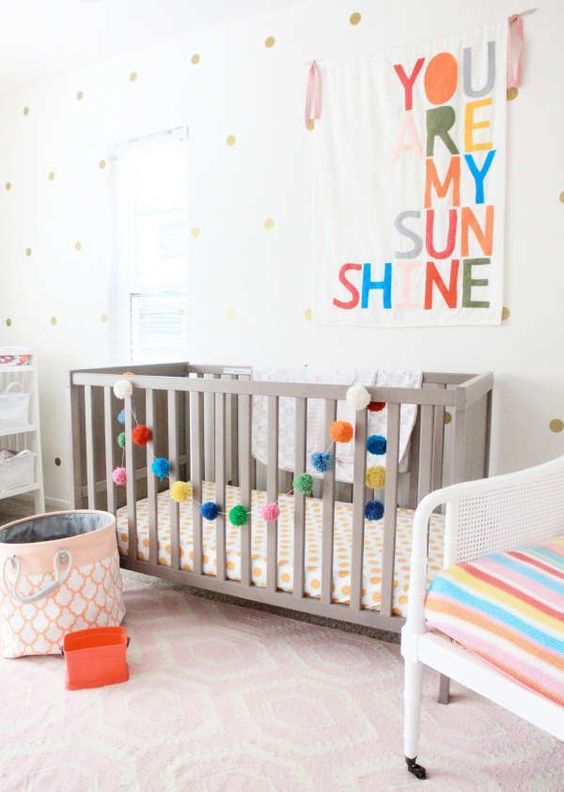 a colorful gender neutral nursery with grey and white furniture, colorful letters and garlands, printed textiles and a polka dot wall