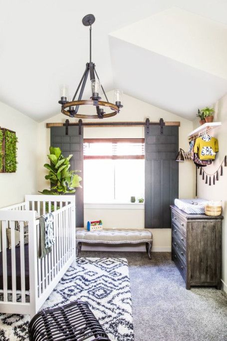 a cozy rustic nursery with a tassel garland, printed rugs, a wooden plank ottoman and much greenery