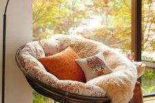 20 a rattan papasan chair with soft upholstery, faux fur and pillows, a floor lamp and bright pillows around for cozy reading