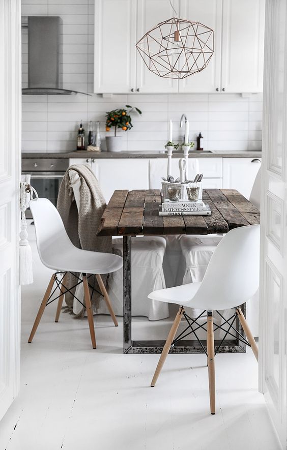 a Scandinavian kitchen in white, with stone countertops, a metal pendant lamp, a rough wooden table, white chairs